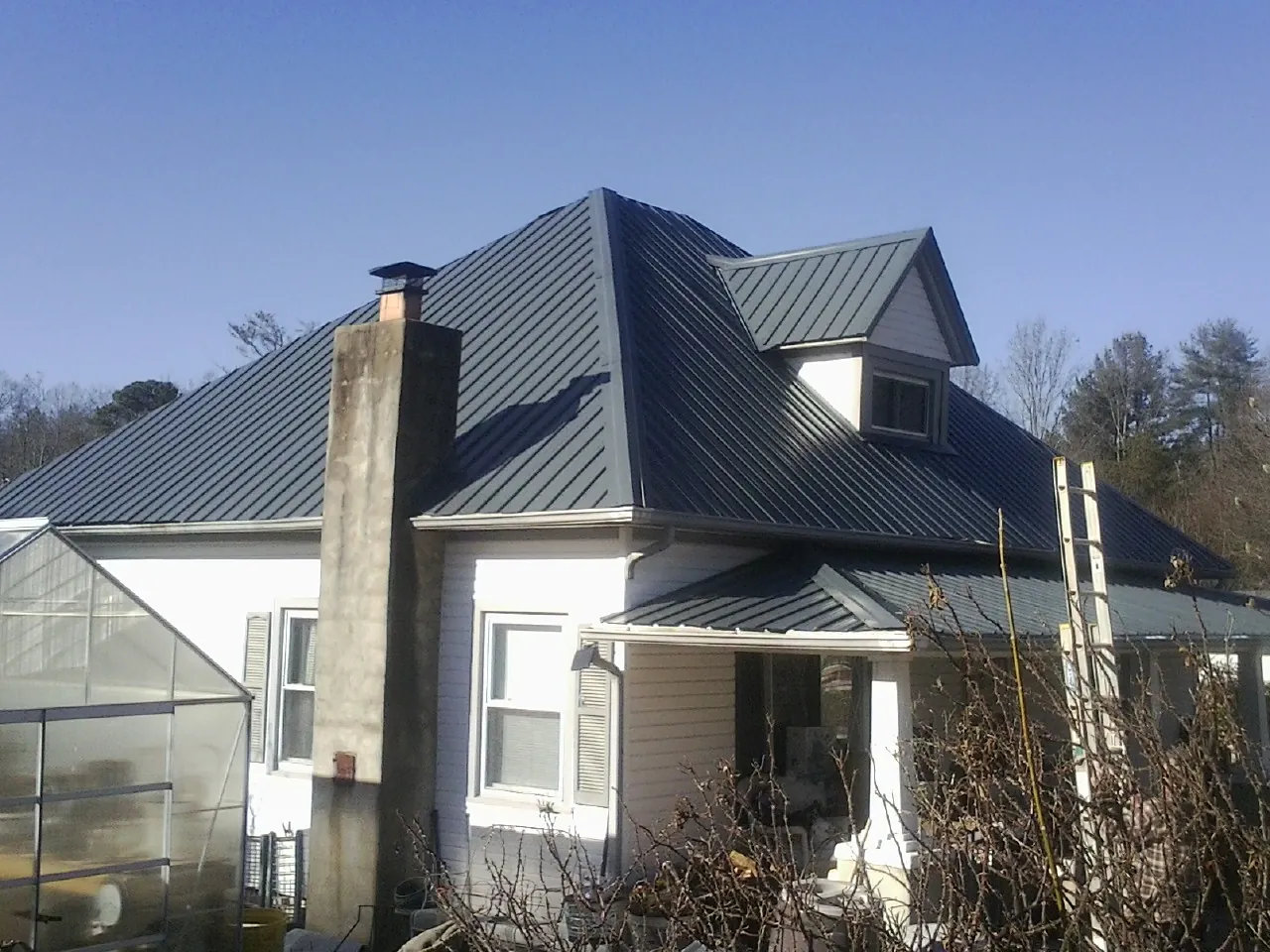 Dark blue standing seam metal roof on a white farmhouse with dormer — Slate & Tile Roof Repair by Roofing Brothers in Winter Park