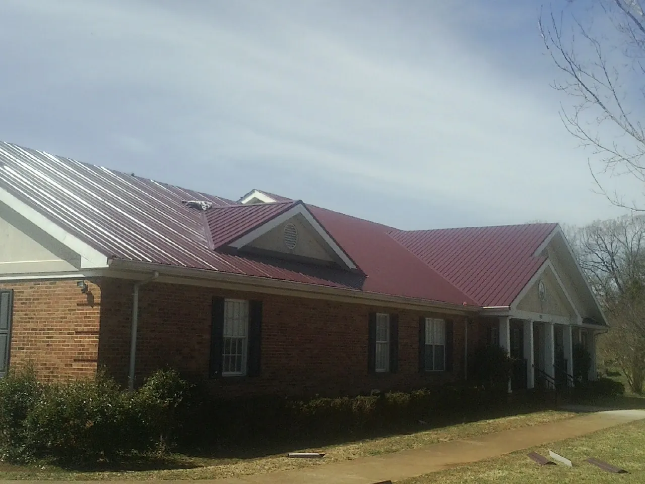 Red metal roof with gabled entries on a long brick building, from a Hail Damage Roof Repair job in Winter Park