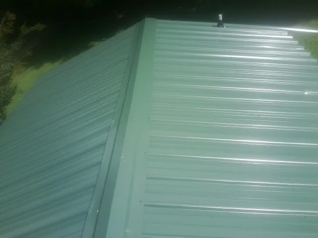 New green metal panels meeting at the ridge of a roof — Flat Roof Repair work by our crew in Winter Park