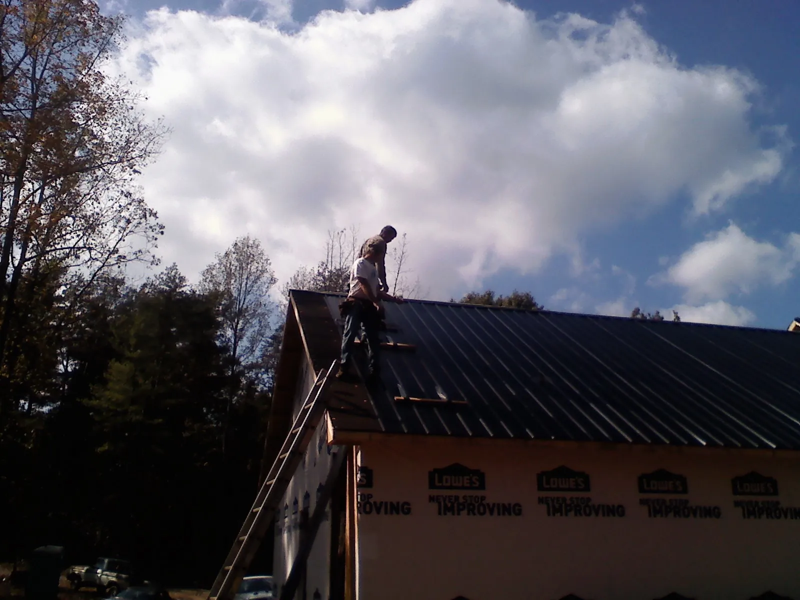 Roofer fastening dark metal panels high against a cloudy sky, from a Roof Inspection job in Winter Park